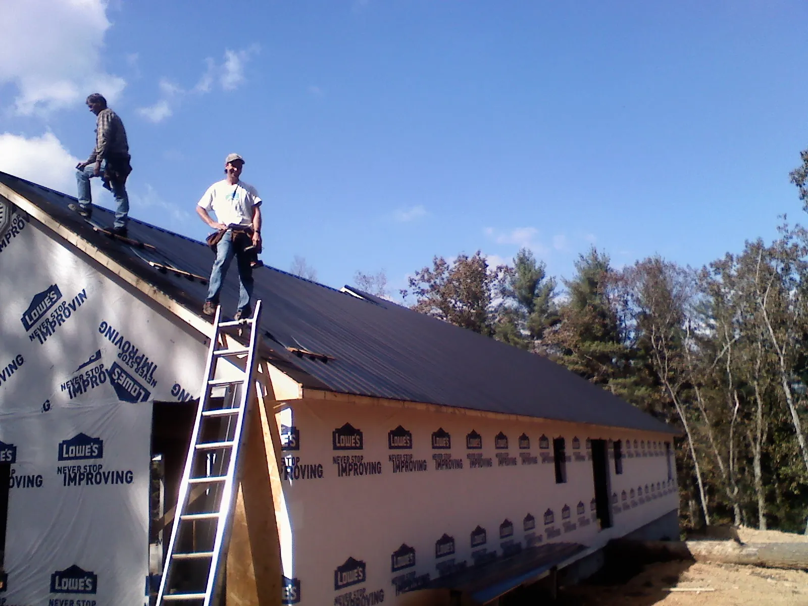 Two roofers standing on a long dark metal roof over a wrapped building in Douglas